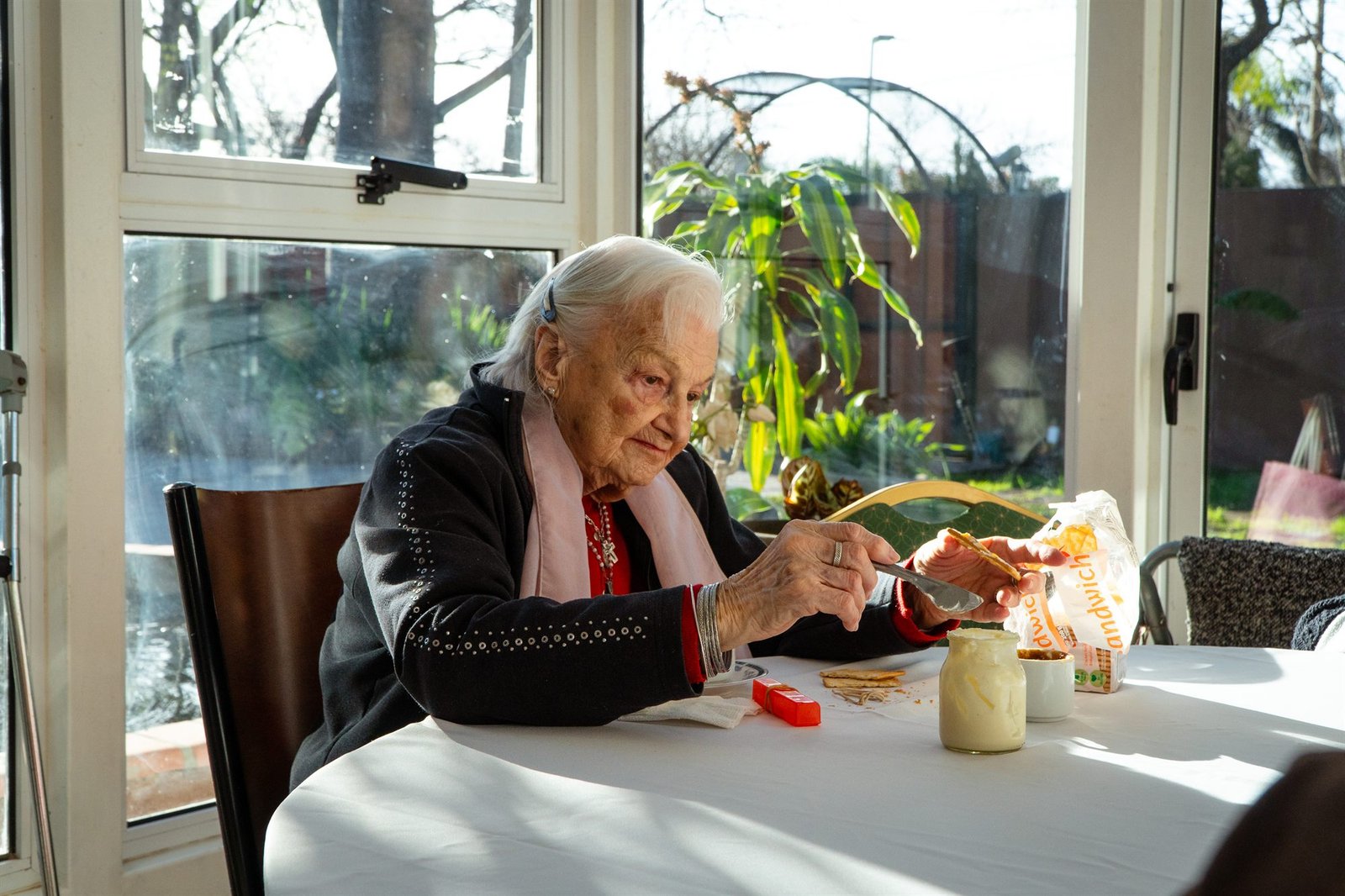 Una residente de Alcanfor prepara su merienda junto al ventanal, con el jardín detrás.
